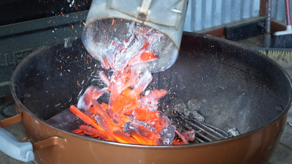 Glowing BAM bamboo charcoal being poured into a kettle grill